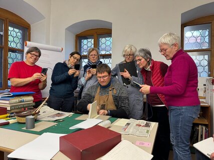 Mehrere Personen stehen um einen Lehrer herum, der etwas an einem Buch zeigt